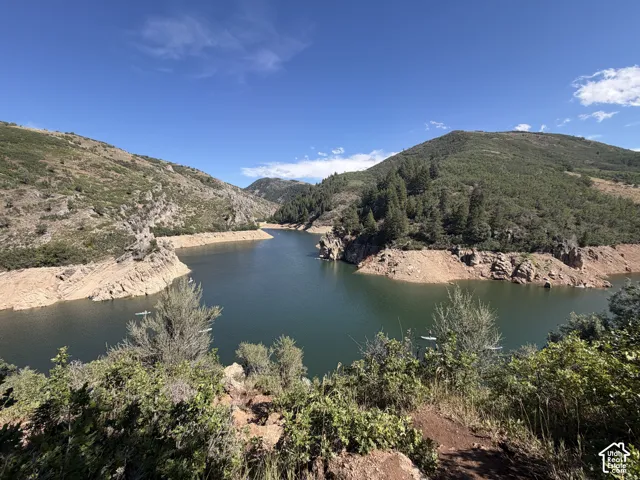 Expansive natural landscape featuring a prominent body of water, rugged mountain terrain, and diverse foliage