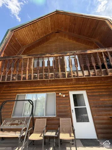 Wood-sided exterior featuring a gabled roofline, second-story balcony with wood railing, and a ground-level covered patio with a white entry door