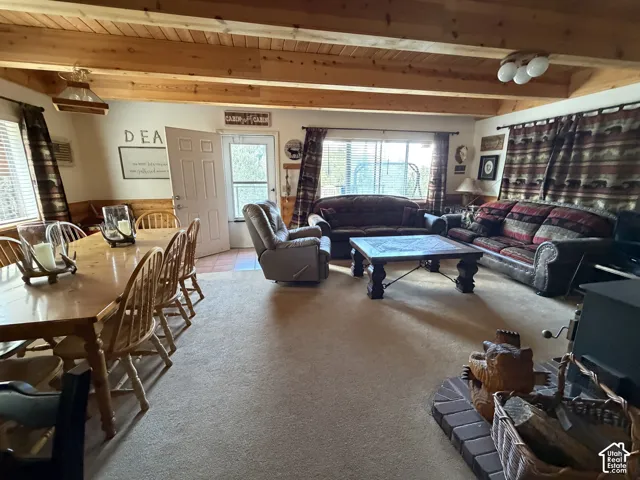Exposed wood beam ceiling, light-toned carpet flooring, window with blinds, and white door