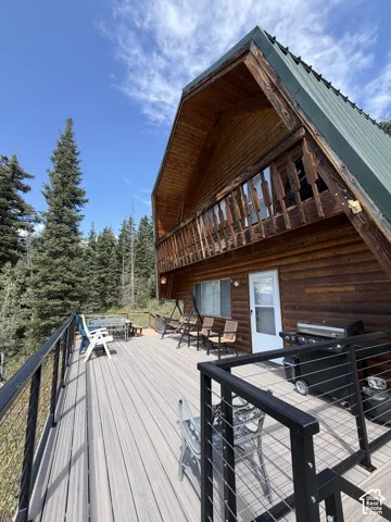 Expansive outdoor deck with composite decking and cable railing, featuring a log cabin exterior with a metal roof and a second-story wood balcony