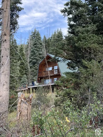 Wood-sided A-frame structure with a green metal roof, multiple windows, and an upper-level balcony