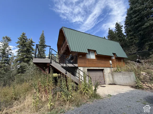 Log-sided exterior with a green metal roof, elevated deck with dark railings, and a lower-level garage with a roll-up door
