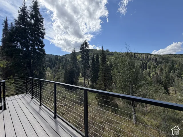 Outdoor deck with composite plank flooring and cable railing system, overlooking a mountainous landscape with mature trees