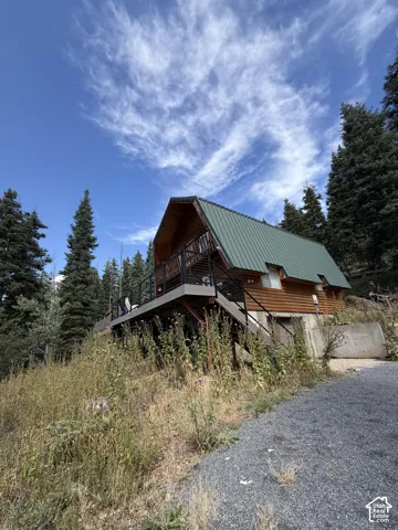 A-frame style residence with wood siding, a green metal roof, an elevated deck, and a gravel driveway