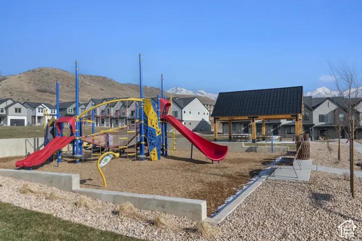 Community playground with multiple slides and climbing features, covered picnic area, concrete pathways, and surrounding natural landscaping