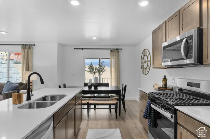 Kitchen featuring light wood-finish flooring, two-tone cabinetry, stainless steel appliances, white countertops, and a black gooseneck faucet