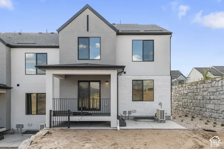 Rear exterior with a covered patio and concrete slab, featuring a textured block retaining wall and dark-framed windows