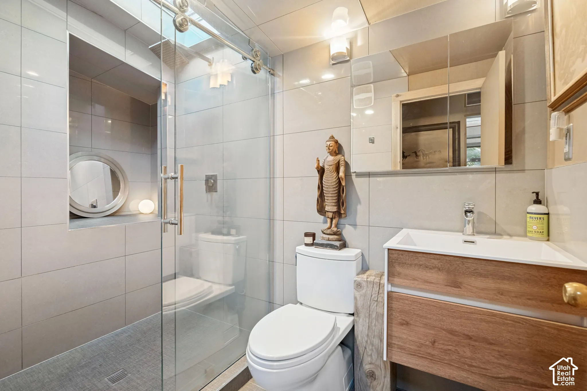 Glass-enclosed shower with a recessed niche, wood-finish vanity with an integrated sink, wall-mounted mirrored medicine cabinet, and tile flooring
