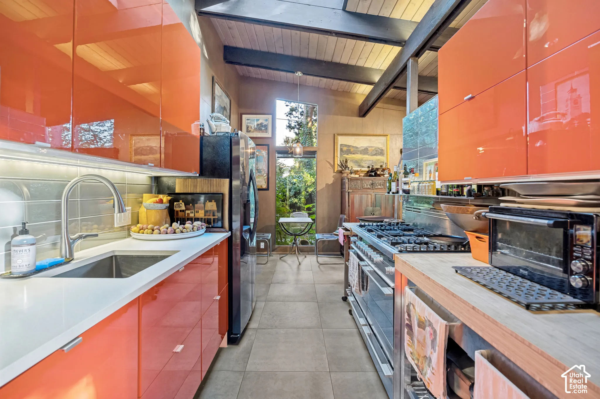 Vaulted wood-paneled ceiling, exposed beam accents, stainless steel range, contemporary orange cabinetry, and large glass pane windows