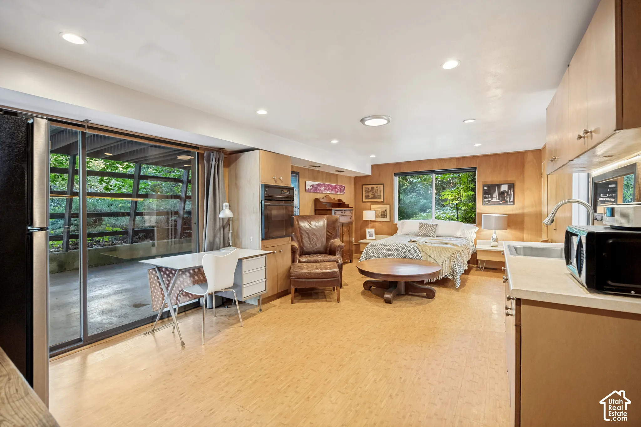 Recessed lighting, wood-finish walls, and a built-in oven, complemented by a sliding glass door and a window overlooking exterior greenery