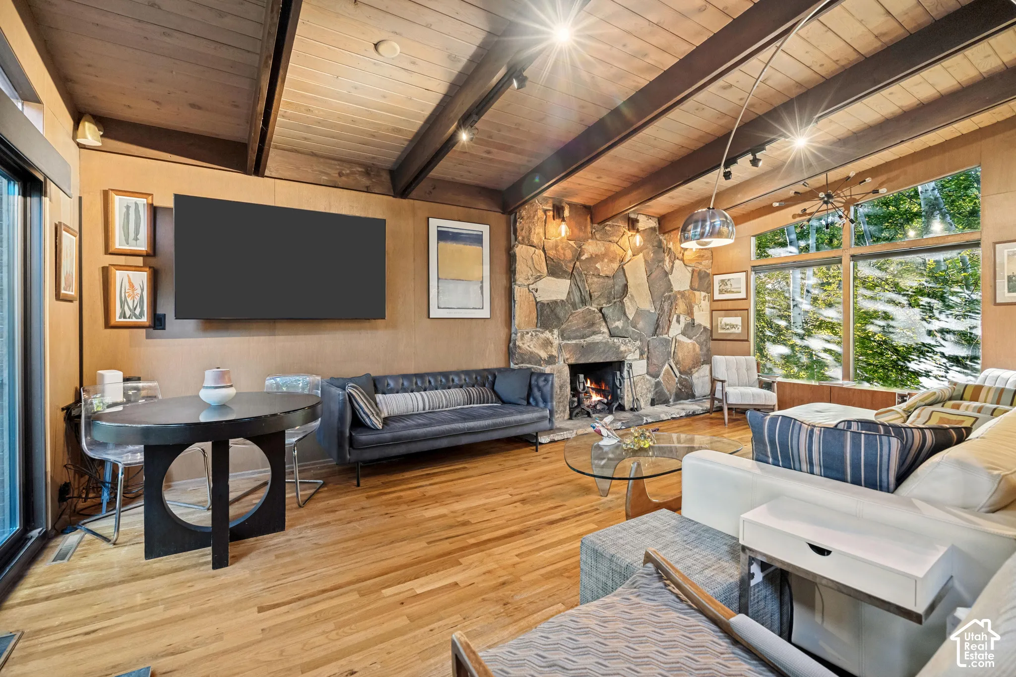 Vaulted wood-paneled ceiling with exposed beams, stone-clad fireplace, large windows, wood-finish flooring, and built-in wall paneling