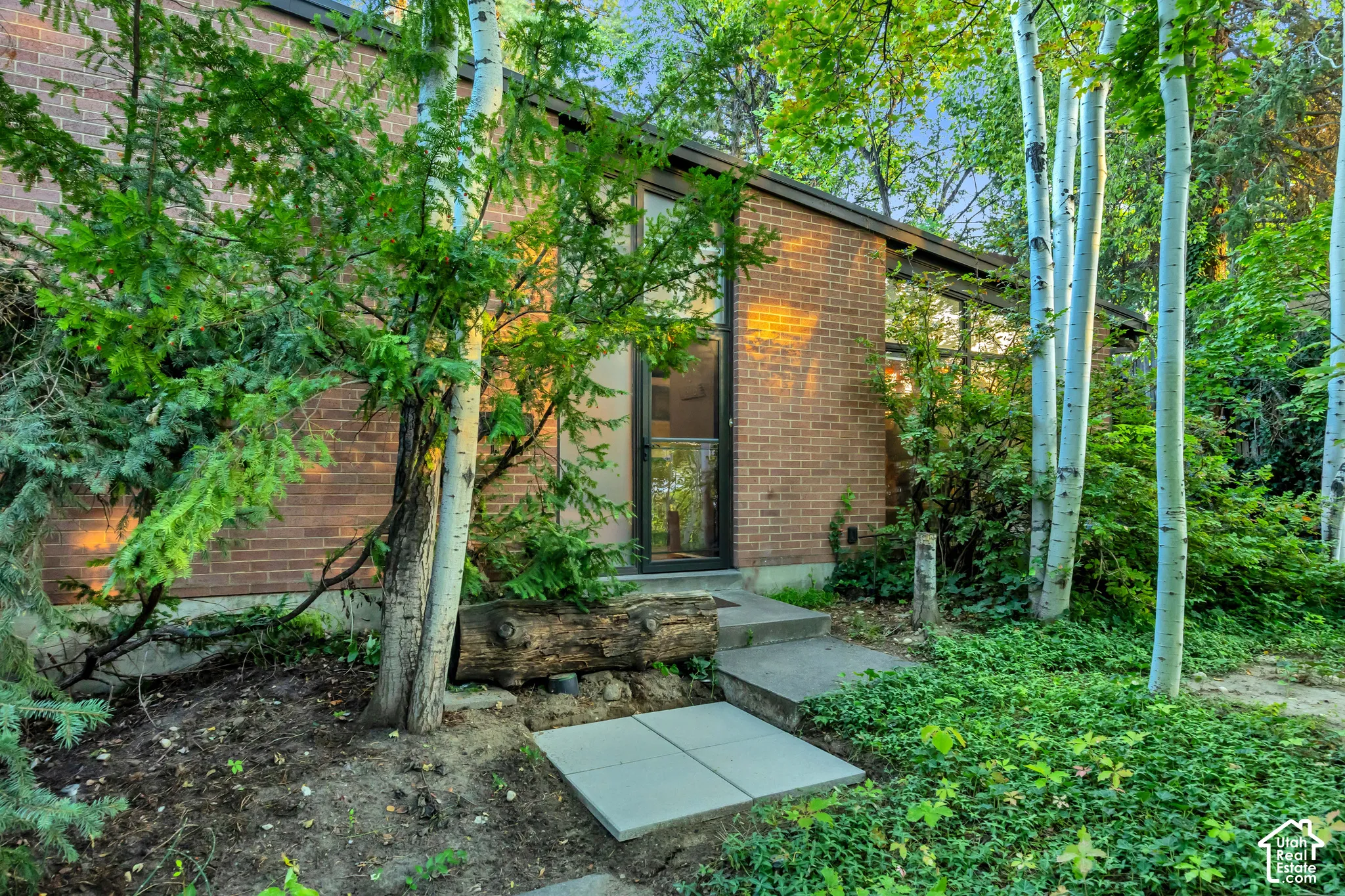 Brick exterior with abundant mature trees and an inviting concrete pathway