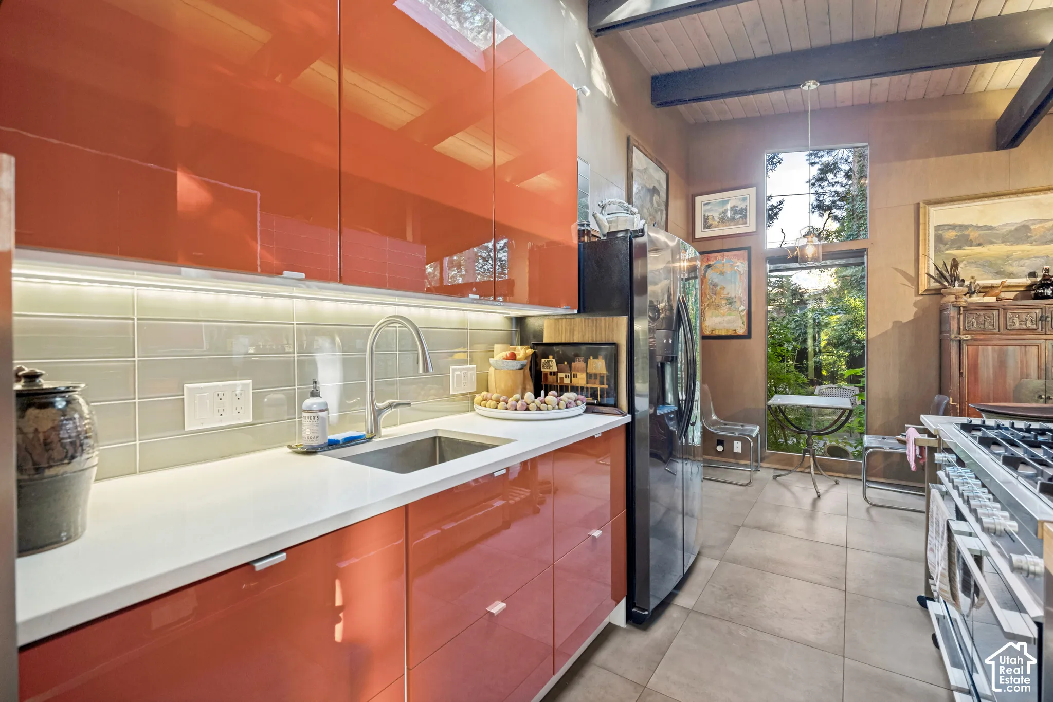 Kitchen featuring high-gloss orange cabinetry, light gray subway tile backsplash, stainless steel sink with gooseneck faucet, and tiled flooring