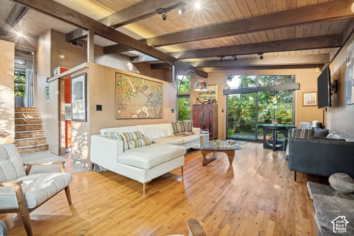 Hardwood flooring throughout, exposed wood beam ceiling, floor-to-ceiling windows, natural wood paneling, and a stone fireplace hearth
