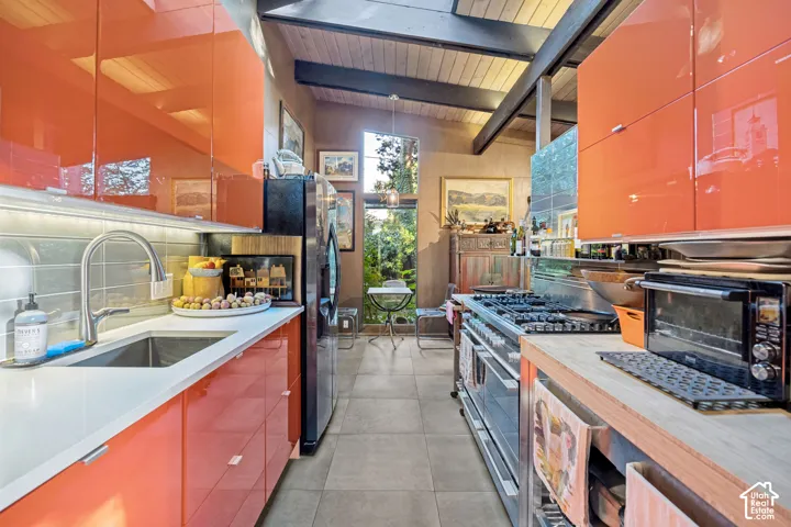 Vaulted wood-paneled ceiling, exposed beam accents, stainless steel range, contemporary orange cabinetry, and large glass pane windows
