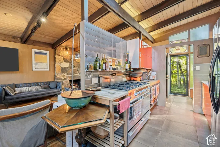 Exposed beam wood ceilings, stone-clad fireplace, integrated gas range with double oven, tiled backsplash, and wood-finish cabinetry