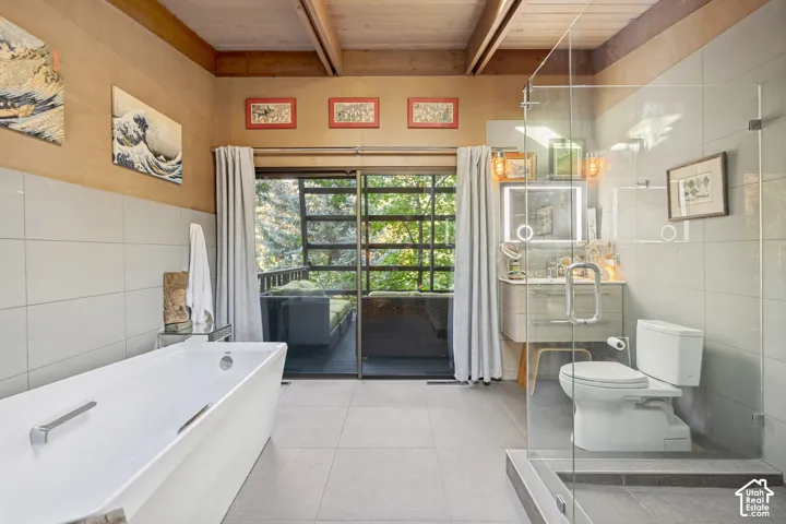 Modern bathroom featuring a freestanding soaking tub, glass-enclosed shower, wood-finish vanity with integrated lighting, and exposed wood beam ceiling