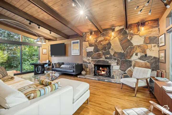 Vaulted wood-paneled ceiling with exposed beams, wood-finish flooring, full-height stone fireplace, and expansive floor-to-ceiling windows