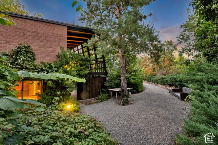 Brick exterior with a covered patio and trellis, complemented by extensive landscaping with mature trees and a gravel pathway