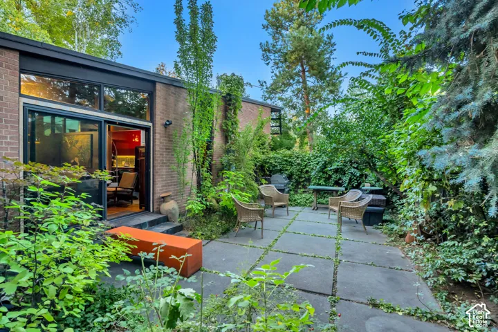 Brick exterior with large windows, sliding glass door, and a stone patio