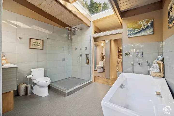 Skylight feature, wood-paneled vaulted ceiling, glass-enclosed shower, large soaking tub, and tile flooring