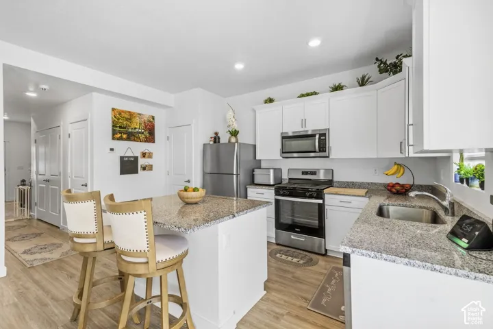 Kitchen featuring white cabinetry, stainless steel appliances, granite countertops, a center island with seating, and wood-finish flooring