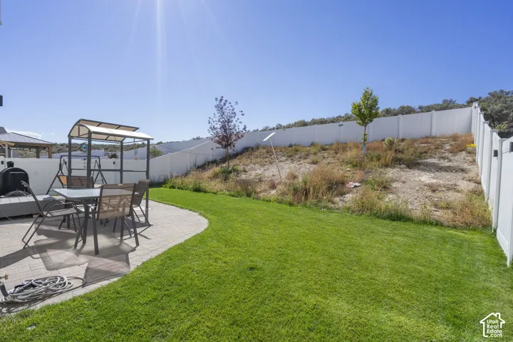Expansive backyard featuring a manicured lawn, a paver patio, a perimeter fence, and a terraced landscape