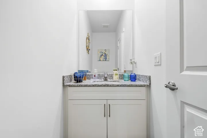 White shaker-style vanity with cabinet storage, granite countertop, undermount sink, and wall-mounted mirror