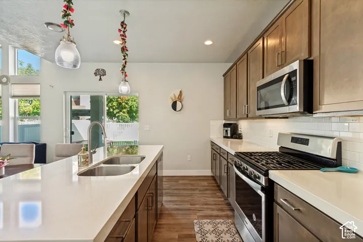 Kitchen featuring wood-finish flooring, white countertops, subway tile backsplash, stainless steel appliances, and wood-finish cabinetry
