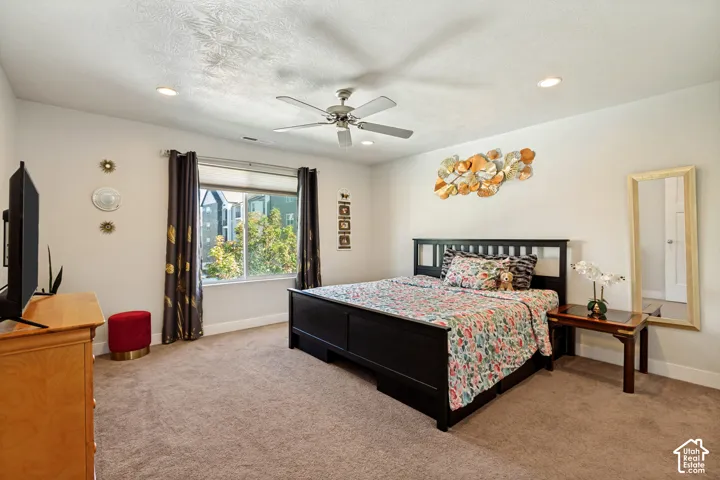 Recessed ceiling lighting, ceiling fan, large window, neutral wall paint, and carpeted flooring