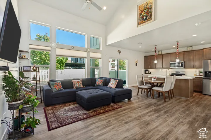 Vaulted ceiling with a ceiling fan, expansive windows, wood-finish flooring, built-in kitchen cabinetry, and stainless steel appliances