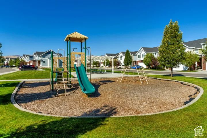 Community park featuring a playground structure with a slide, a separate climbing structure, wood chip ground cover, and surrounding green lawn