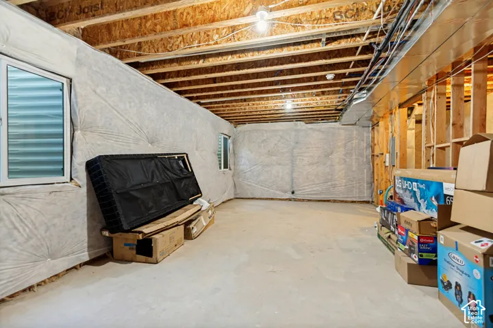 Unfinished basement with concrete flooring, exposed wood joists, and two basement windows