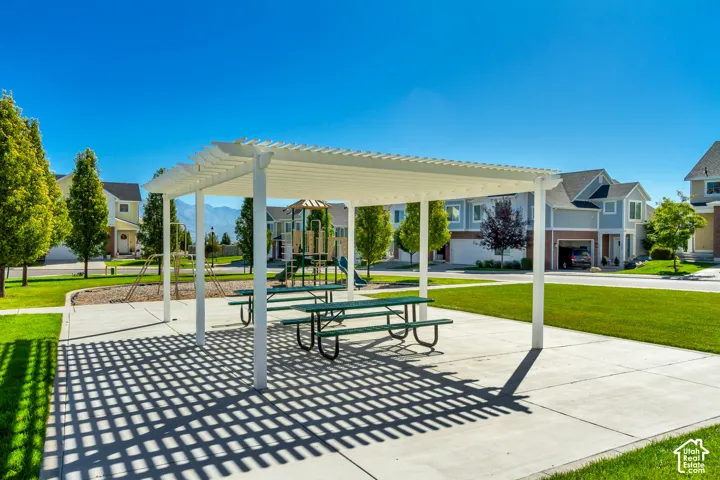 Outdoor pergola structure over a concrete patio with picnic tables, surrounded by manicured lawns and mature trees