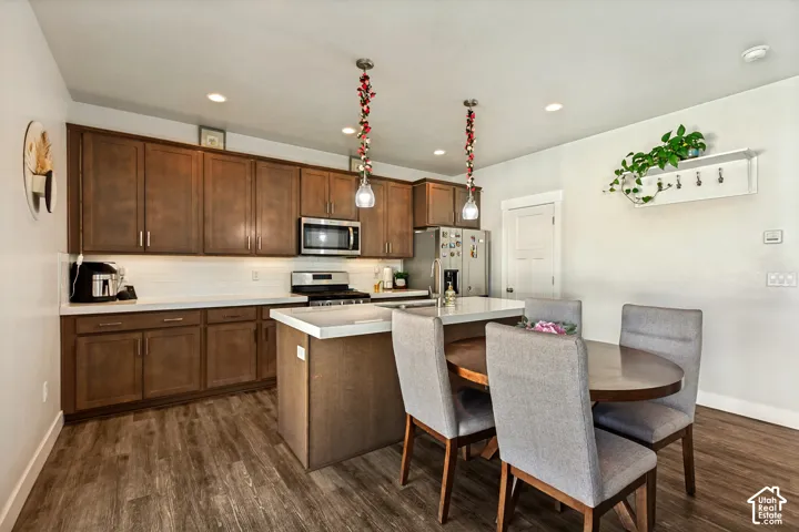 Kitchen featuring wood-finish flooring, stainless steel appliances, white subway tile backsplash, and an island with a white countertop
