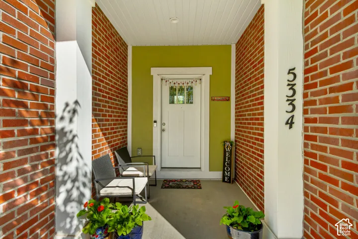 Brick facade entry with white columns, a beadboard ceiling, and a paneled front door