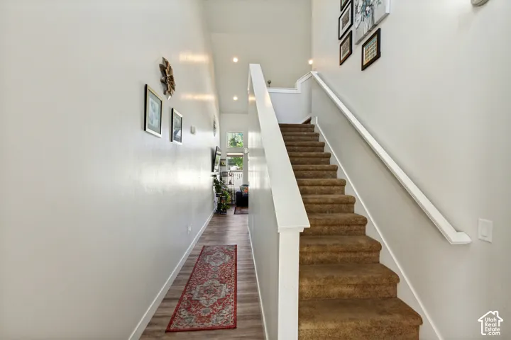 Staircase with carpeted treads and white wood-finish handrail, wood-finish flooring, and recessed ceiling lighting