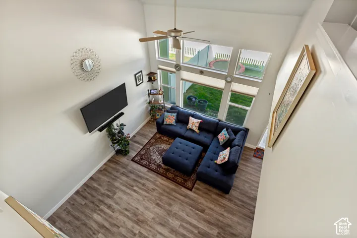 Vaulted ceiling with a ceiling fan, wood-finish flooring, and multiple windows with roller shades
