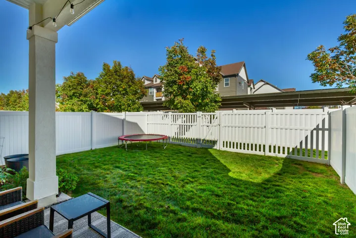 Fenced backyard featuring a manicured lawn, established landscaping, and a covered patio area
