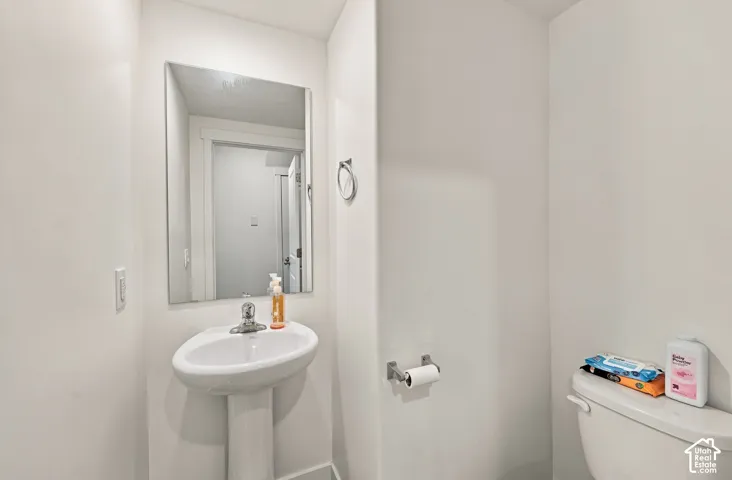 Pedestal sink with a polished chrome faucet, rectangular wall-mounted mirror, and white toilet