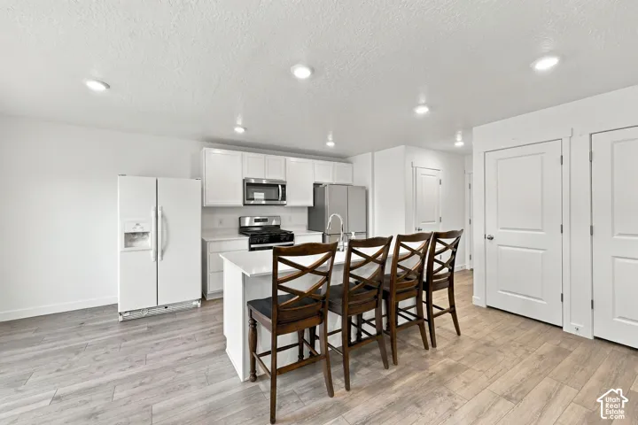 Kitchen featuring an island with seating, white cabinetry, stainless steel appliances, and light wood-finish flooring