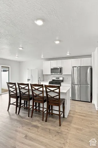 Kitchen featuring white cabinetry, stainless steel appliances, a center island with countertop seating, recessed lighting, and wood-finish flooring