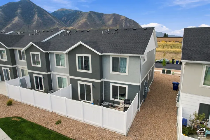 Modern townhome exterior with a dark gray shingle roof, light gray and dark gray stucco siding, white window trim, and a private fenced patio