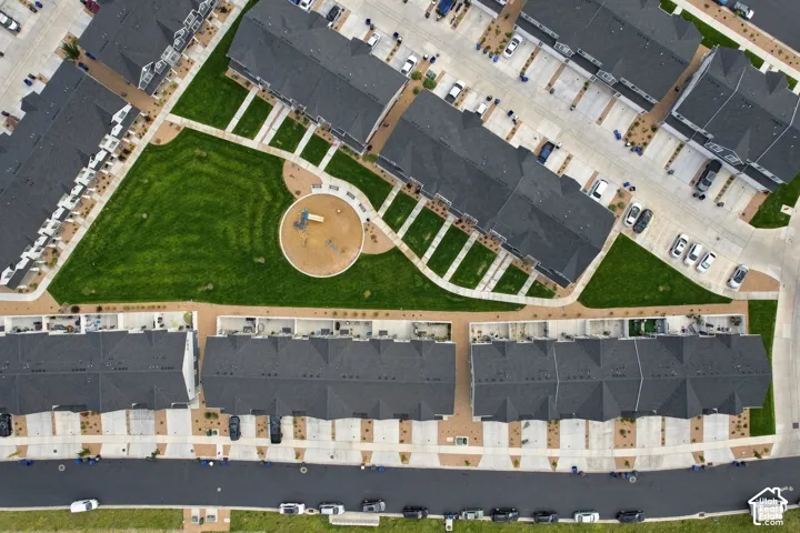 Aerial perspective of a multi-unit property featuring dark-toned roofs, a central green space with a circular paved area, and surrounding paved pathways