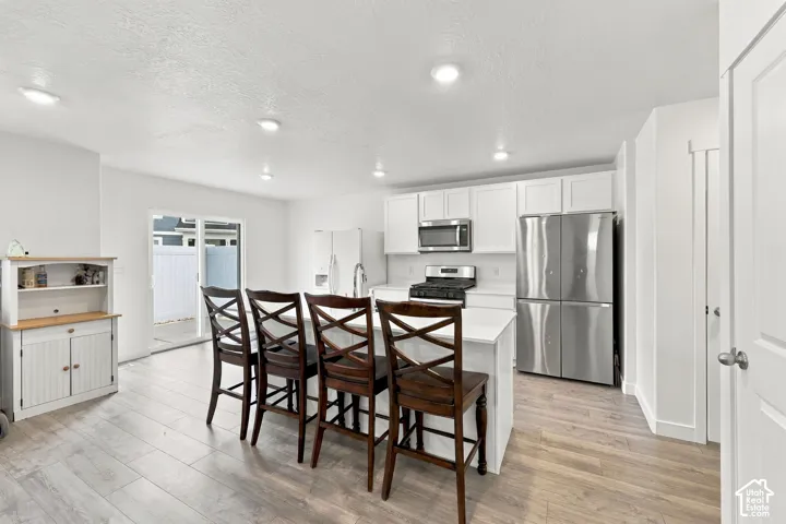 Kitchen featuring white cabinetry, stainless steel appliances, an island with countertop seating, recessed lighting, and wood-finish flooring