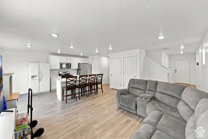 Open-concept living area featuring wood-finish flooring, recessed lighting, and a kitchen with white cabinetry and stainless steel appliances