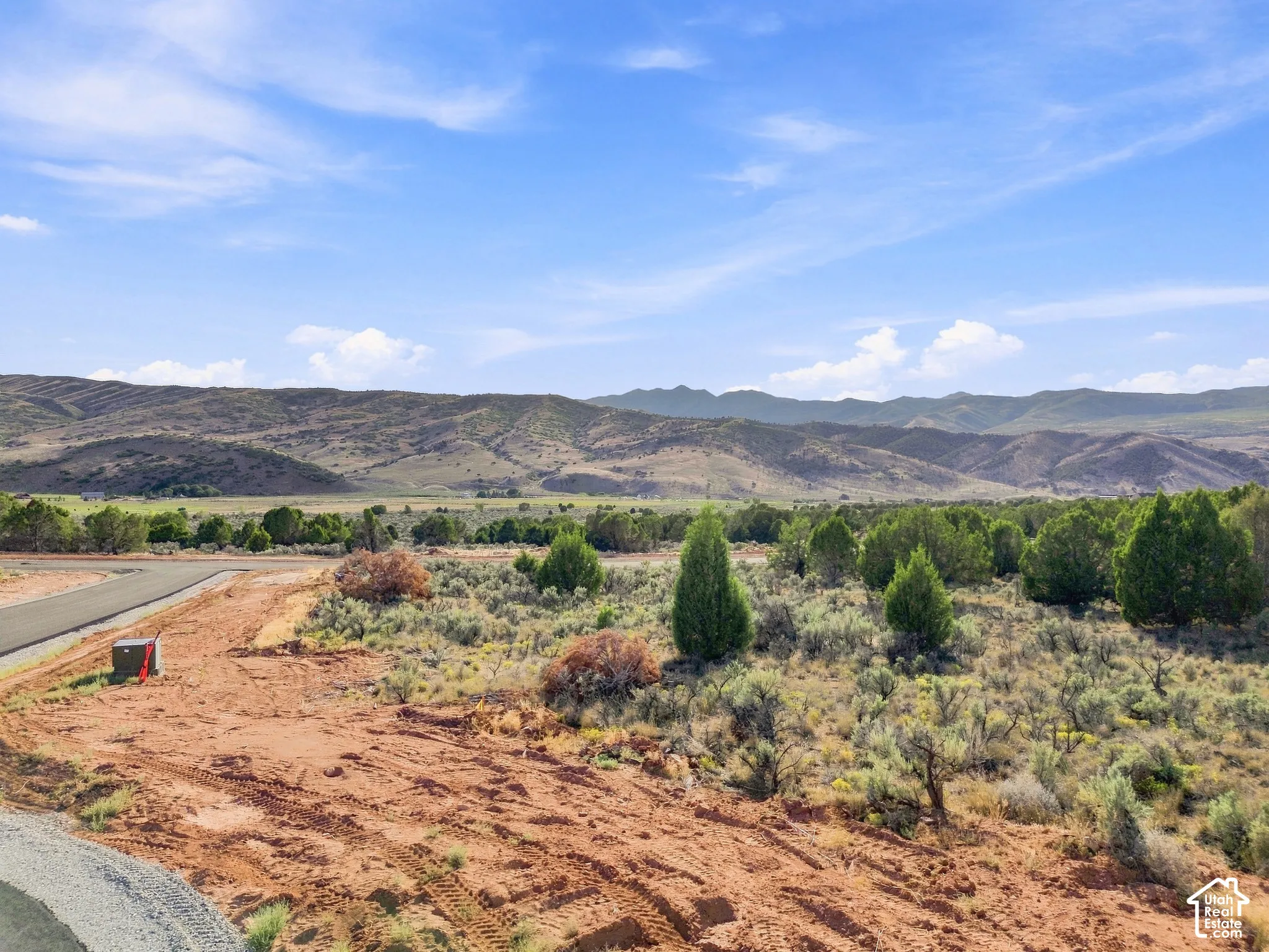 Expansive land with natural vegetation, distant mountains, and partially paved road access