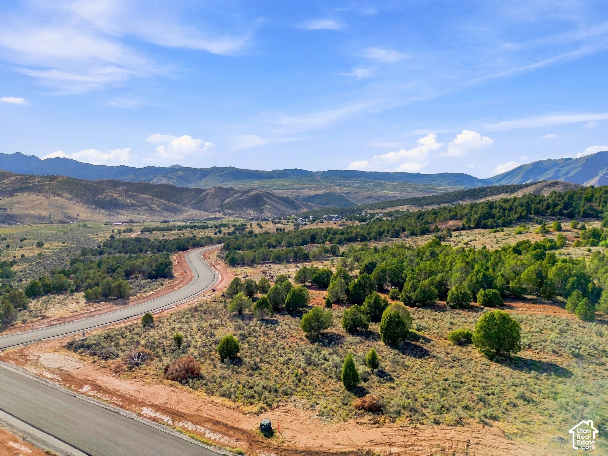 Winding paved road through natural landscaping, surrounded by expansive hills and mountainous terrain under a clear sky