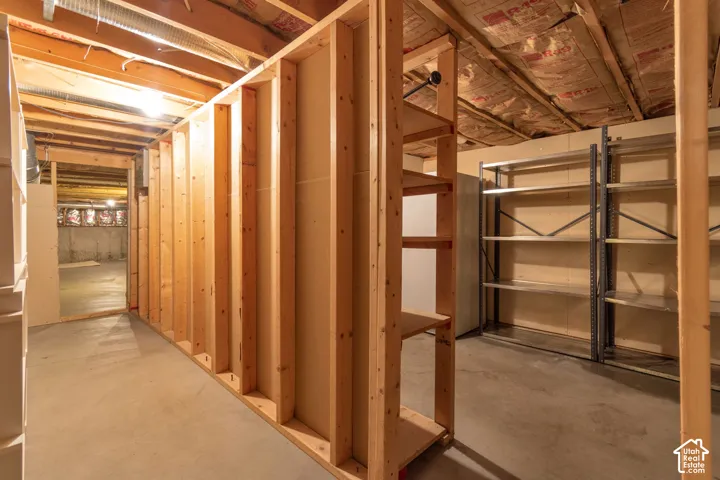 Unfinished basement space featuring exposed wood-frame construction, concrete flooring, and metal shelving units