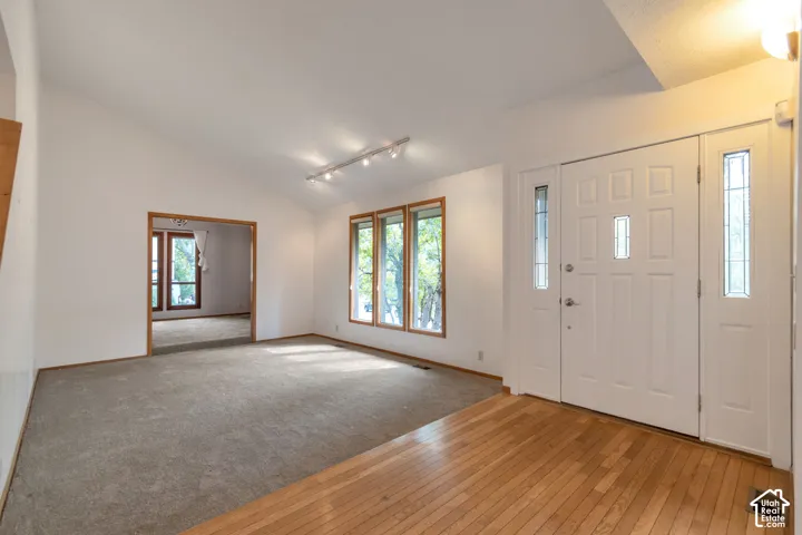 Bright foyer and living area showcasing warm wood-finish flooring, recessed ceiling lighting, and expansive windows with natural light